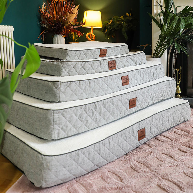 Stack of quilted mattress toppers on a pink surface with a home interior background