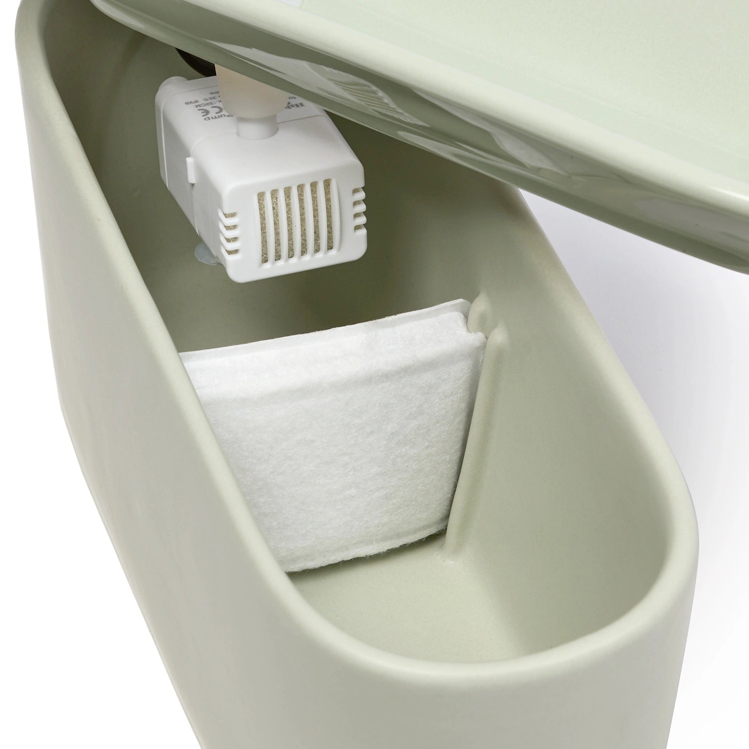 A angled view of the Cat Mate Ceramic Cat Water Fountain in sage green displaying the internal components of the fountain which are the white filter pad and the white filter motor, on a white background.