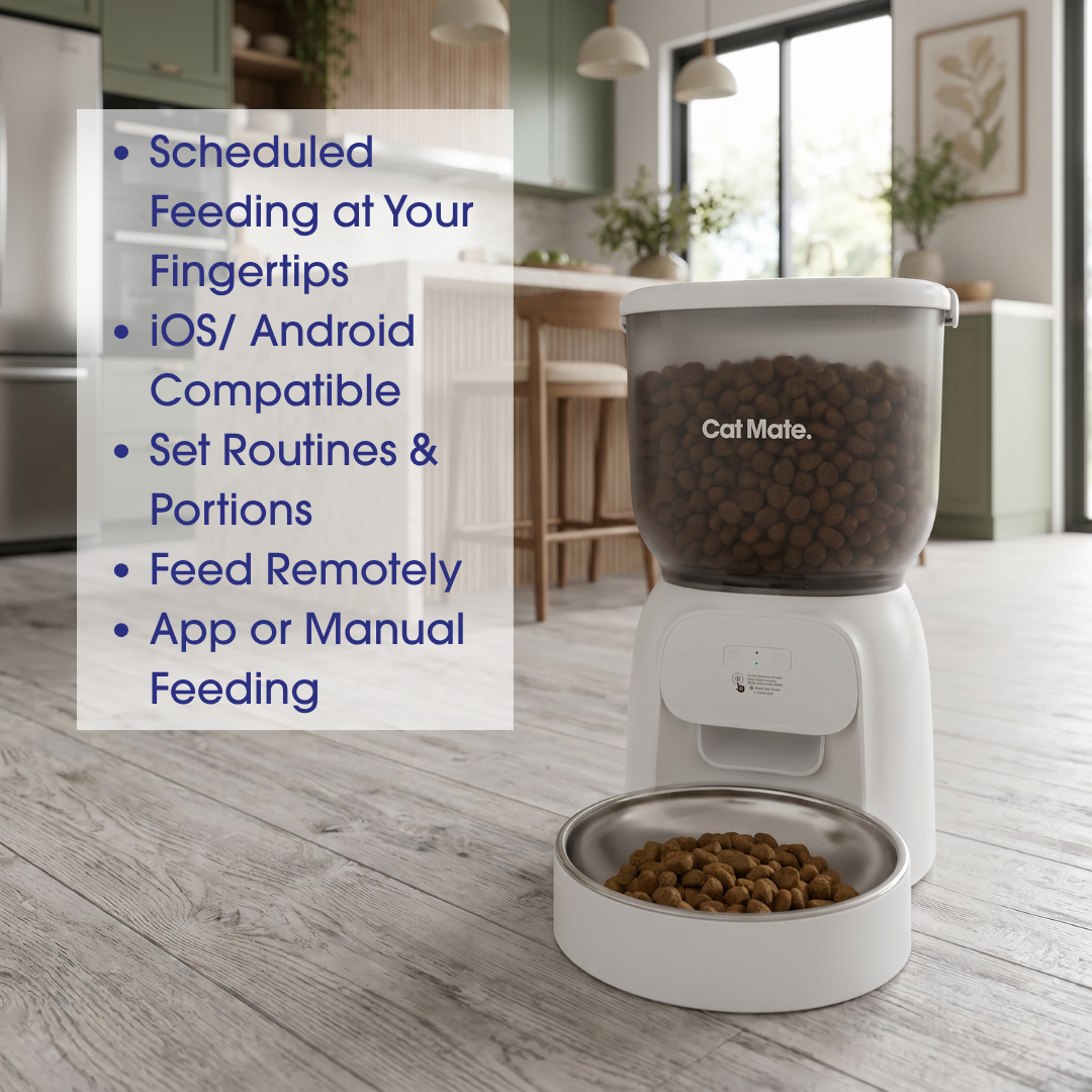 A Cat Mate automatic pet feeder for dry food with a clear container filled with kibble and a stainless steel bowl, shown on a light wood floor in a modern kitchen setting. A text overlay on the left lists features like scheduled feeding at your fingertips and iOS/Android compatibility.