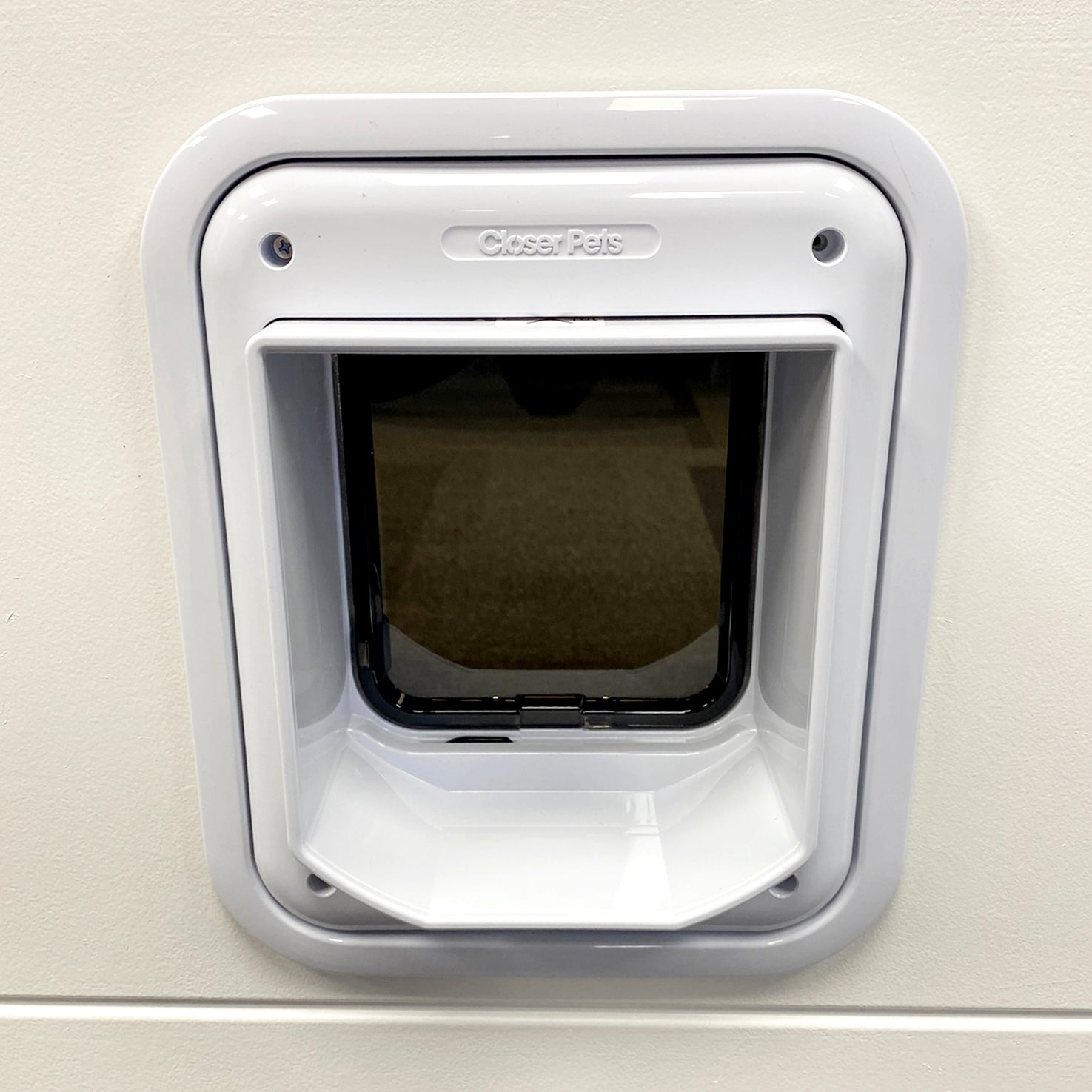 A lifestyle image of the rear of a white cat flap that has been installed in to a white wall using a white cat flap adapter